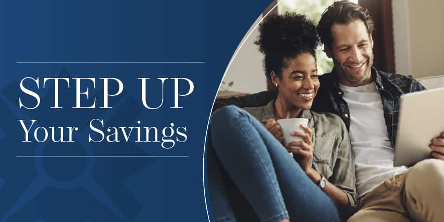 A middle-aged couple sitting on a couch comfortably looking at a tablet. The words at the left: step up your savings.