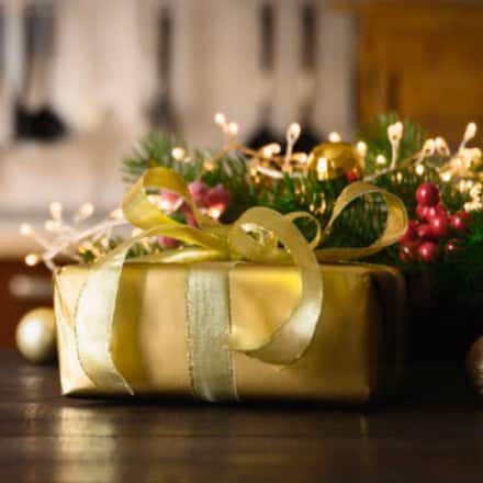 An up close image of a beautifully wrapped gold present with Christmas decor in the background.
