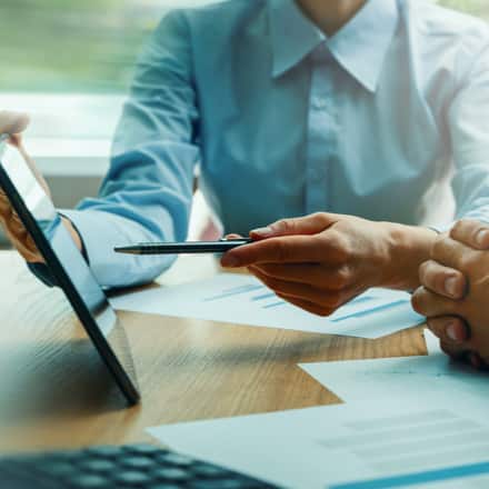 A financial advisor sitting with a client while pointing to a tablet.