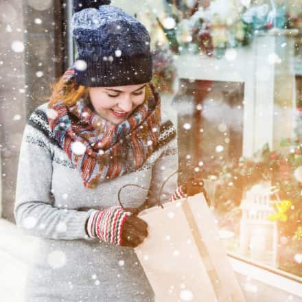 A smiling woman in a wintery setting looking inside a shopping bag.