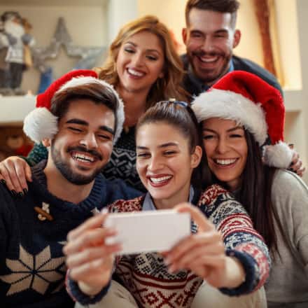A group of smiling friends taking a selfie with holiday decor in the background.