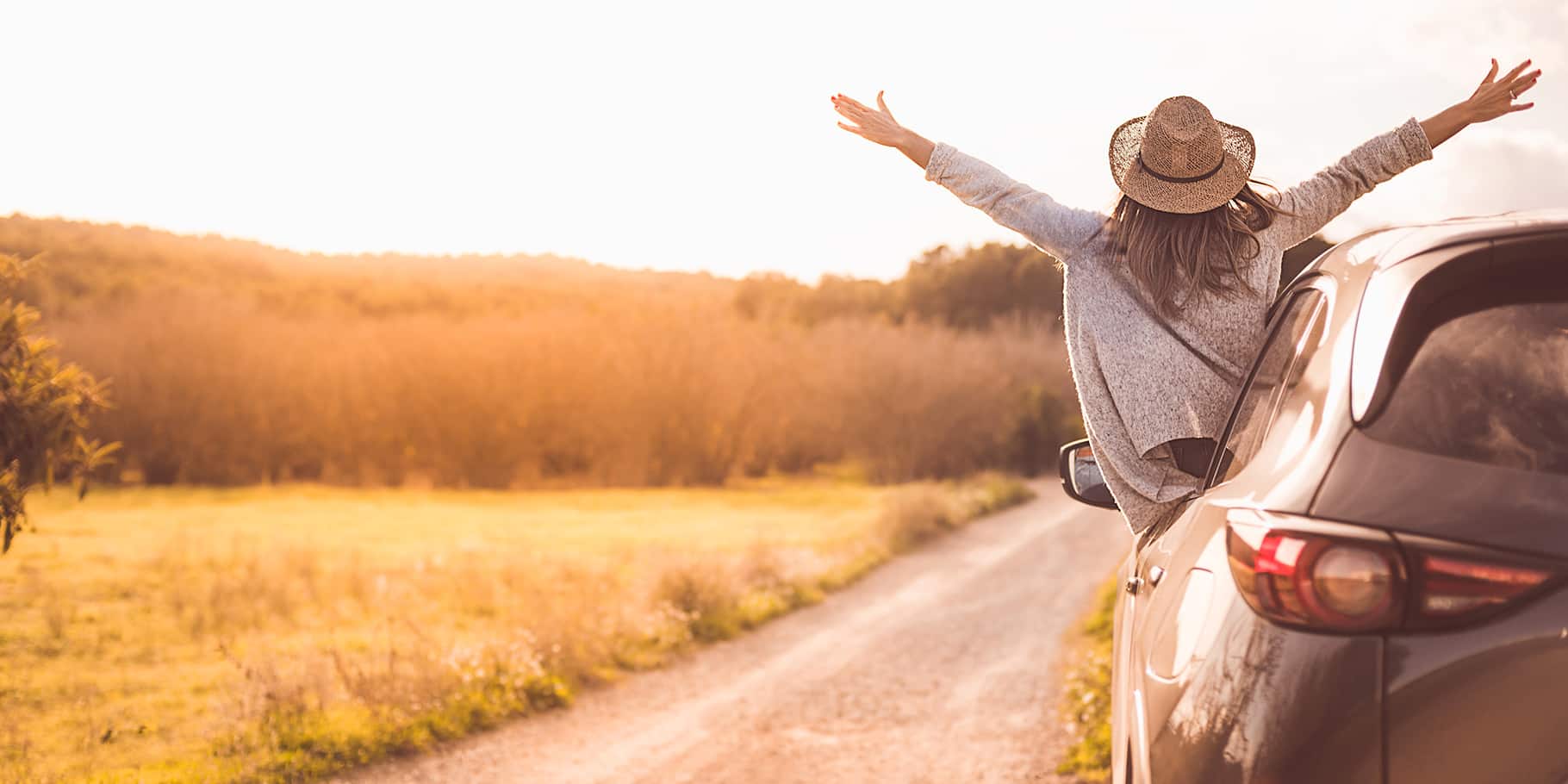 A woman leaning out of a car window with outstretched arms.