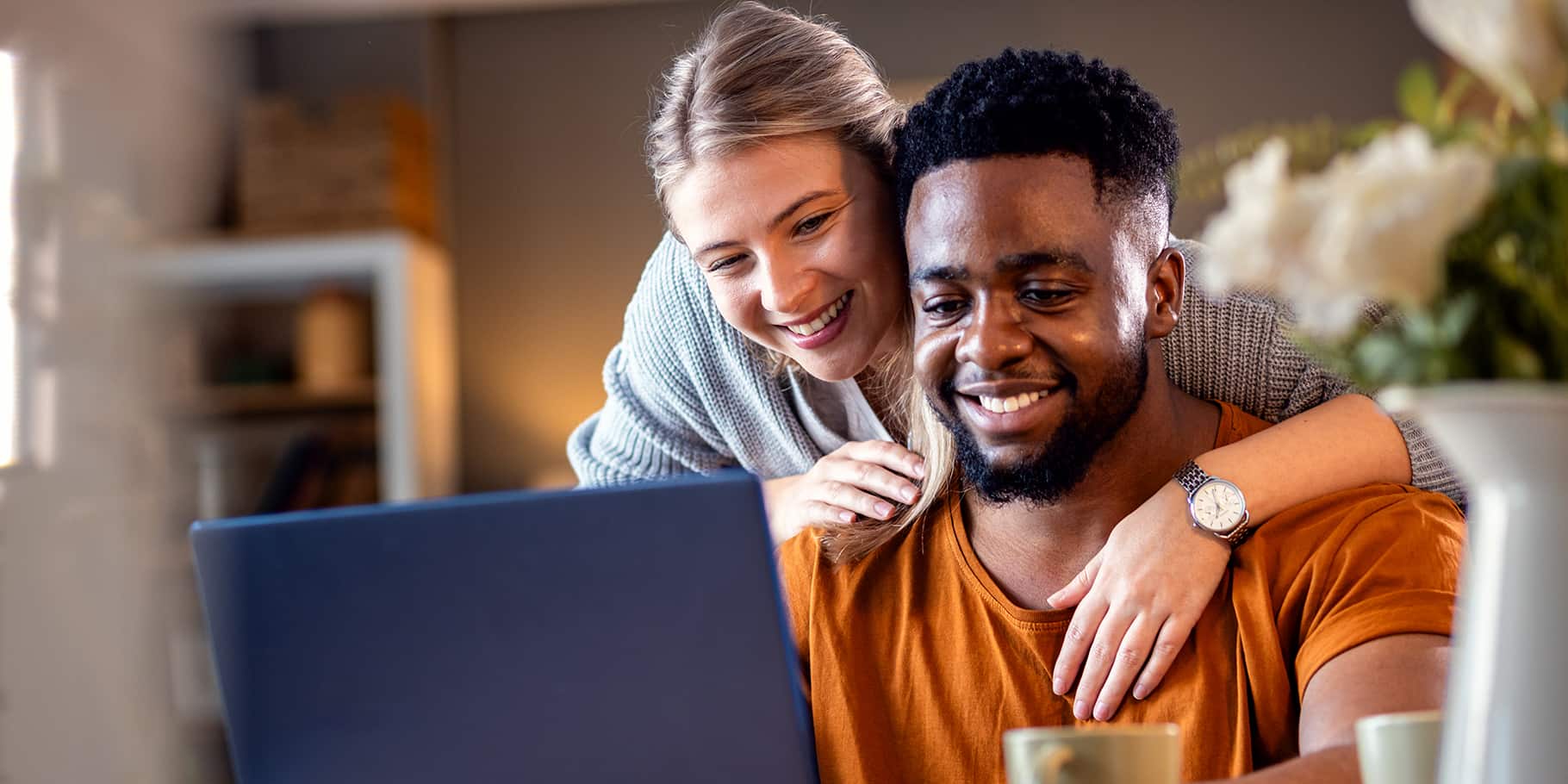 A woman looking over the shoulders of a man who sits using a laptop.