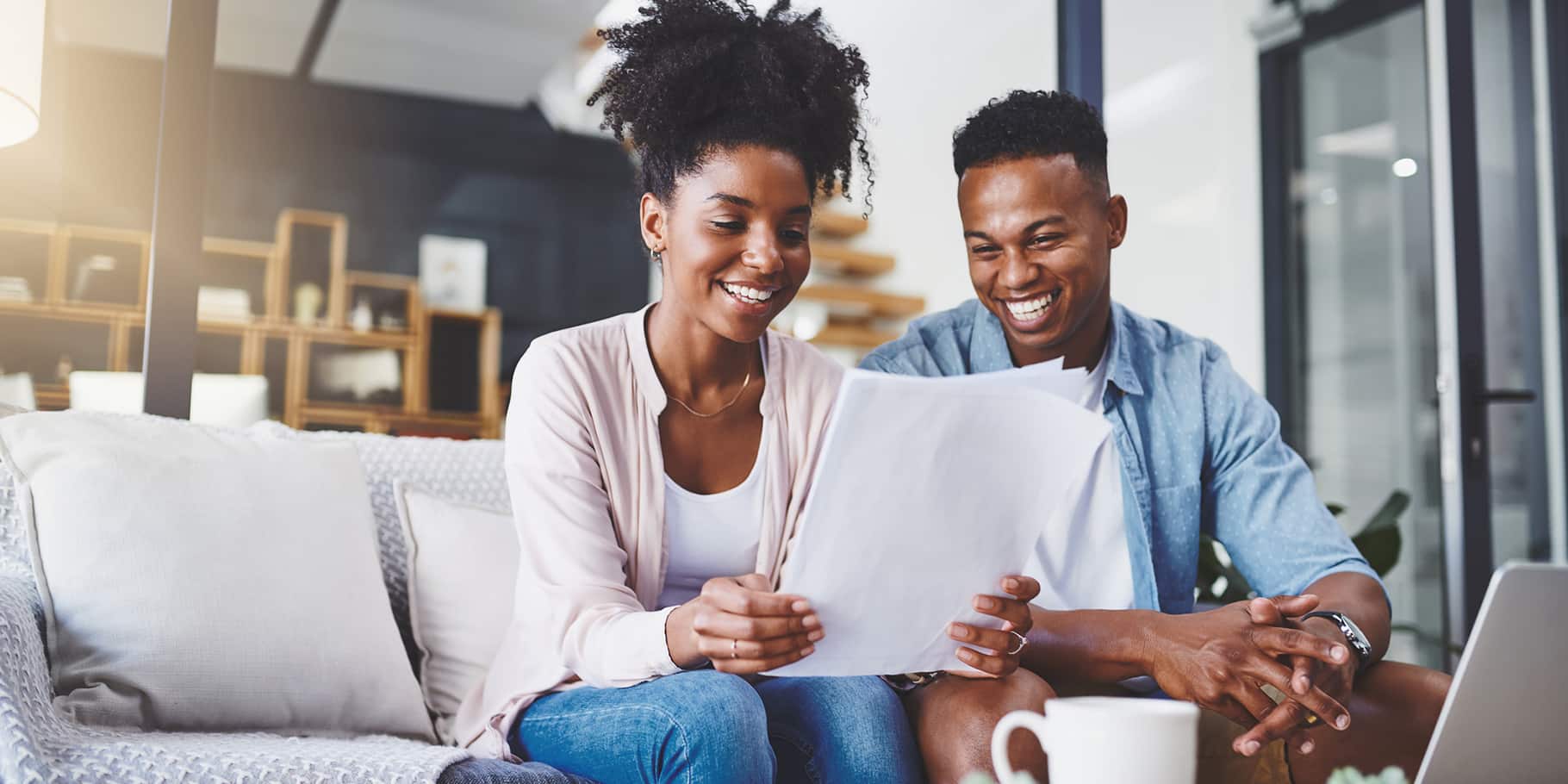 A couple sitting on a couch, smiling and looking at documents.