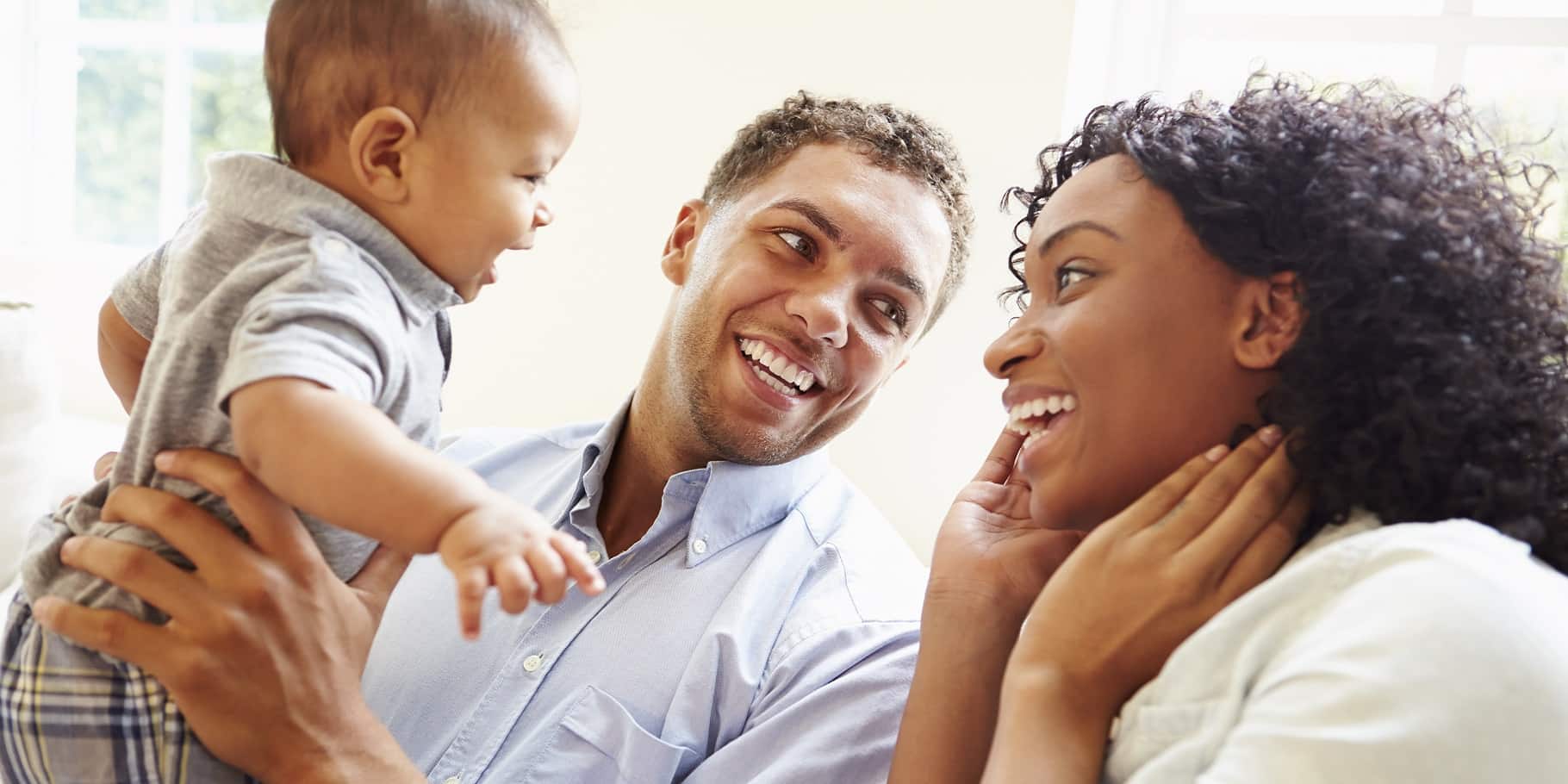 A young couple smiling while the man holds a toddler.