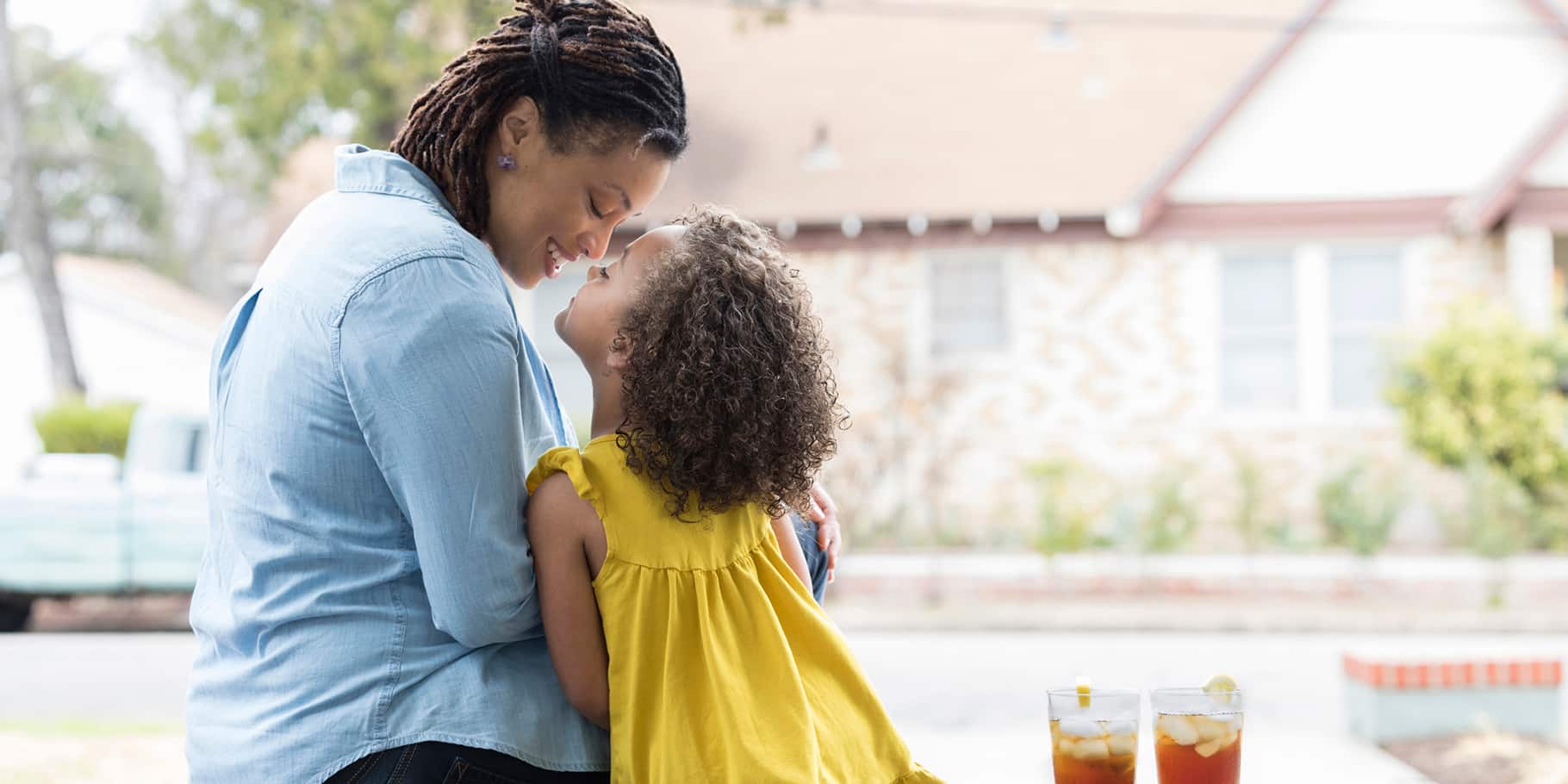 A mother and a young daughter sit and cuddle together on a patio.