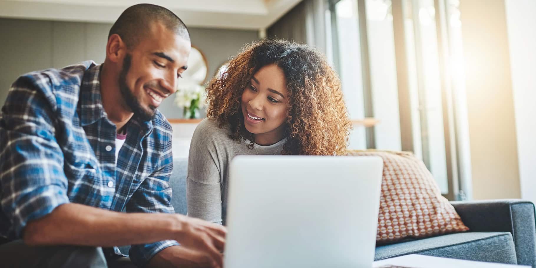 Two young adults sitting on a couch looking at a laptop.
