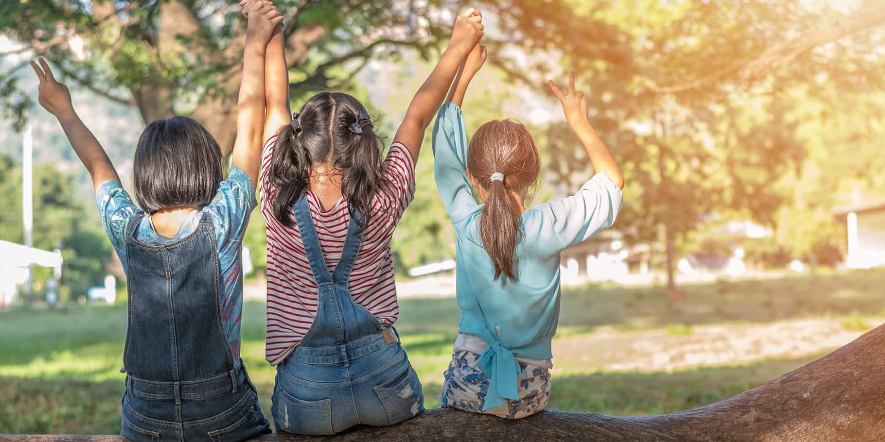 Three young girls sitting together, holding hands and with outstretched arms.