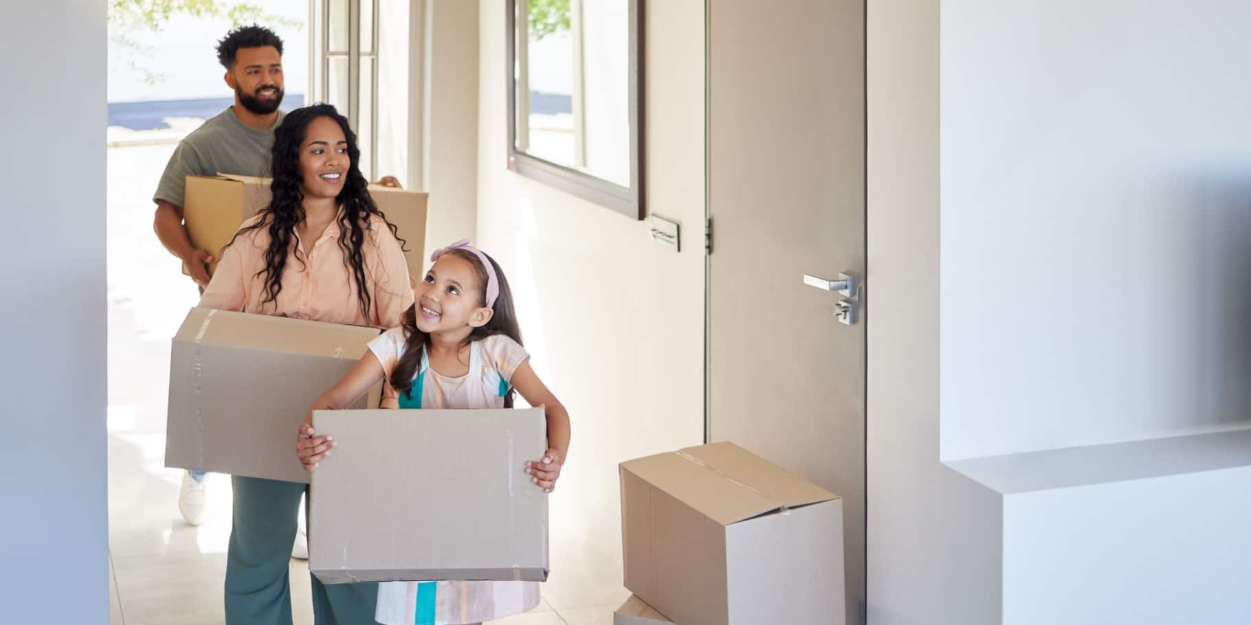 A happy diverse family walking into their home holding moving boxes.