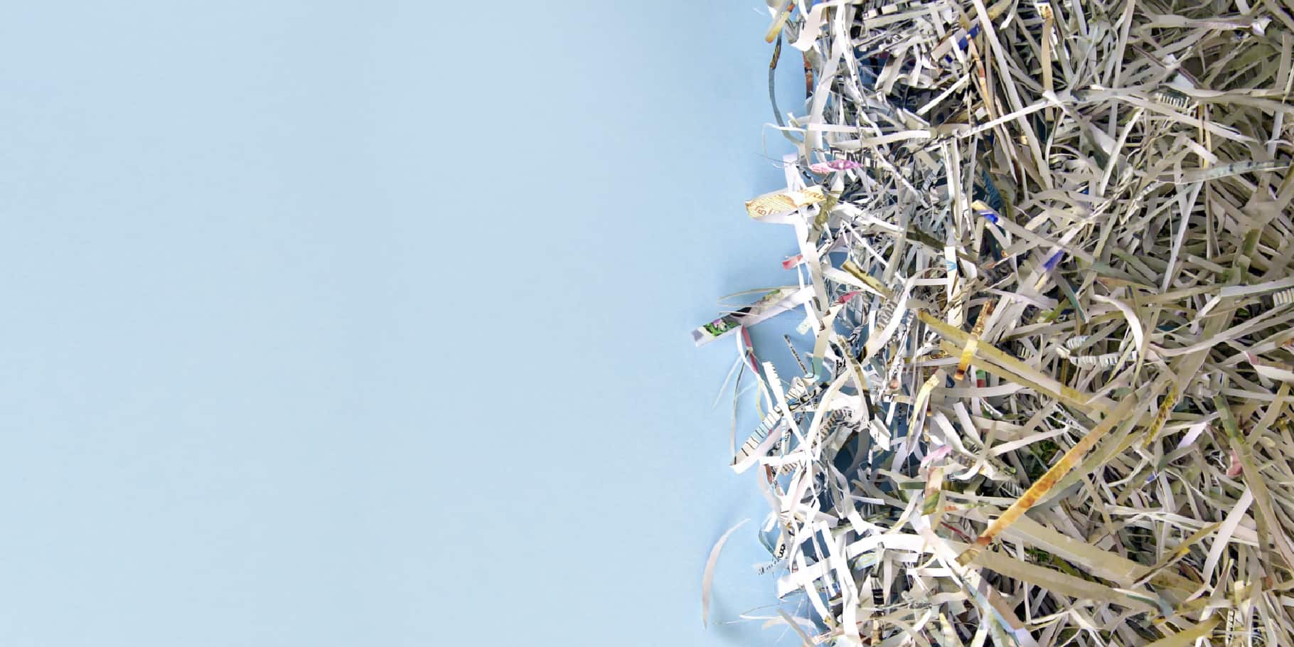 Close-up of shredded paper and mixed recyclable materials piled against a light blue background.