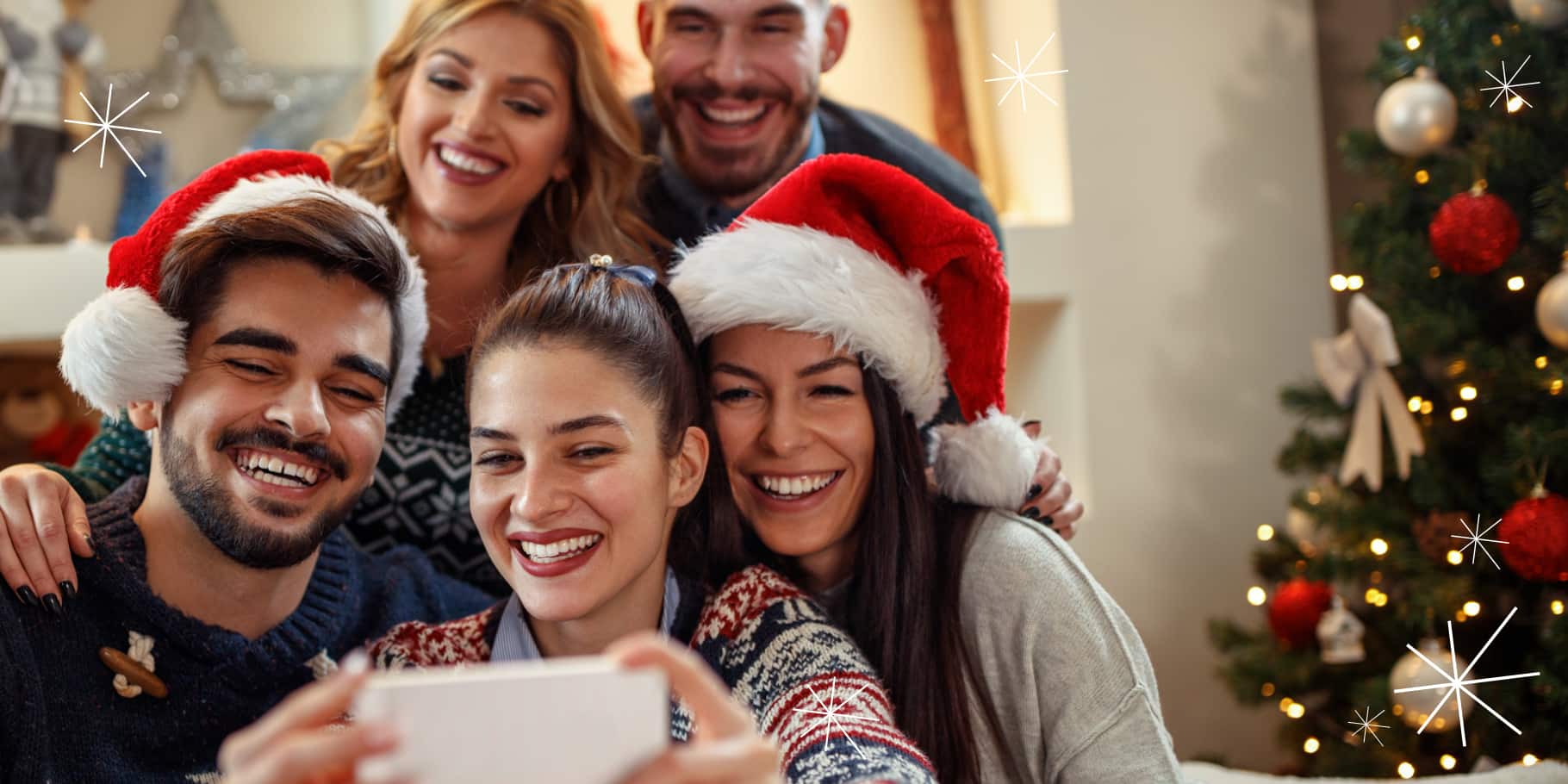 A group of smiling friends taking a selfie with holiday decor in the background.