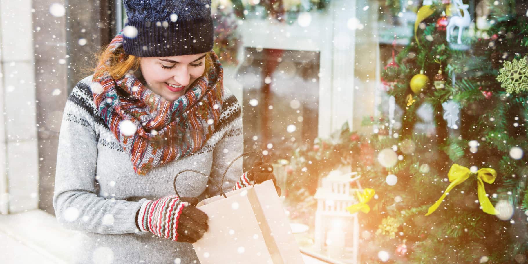 A smiling woman in a wintery setting looking inside a shopping bag.