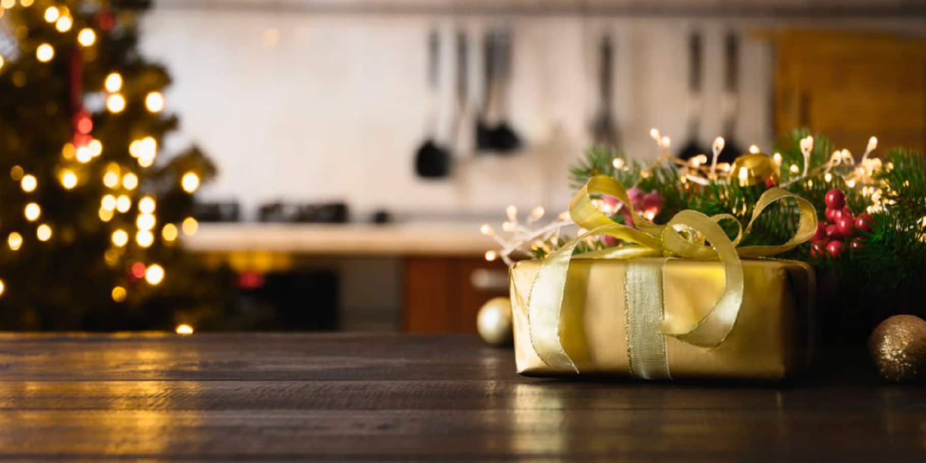 An up close image of a beautifully wrapped gold present with Christmas decor in the background.