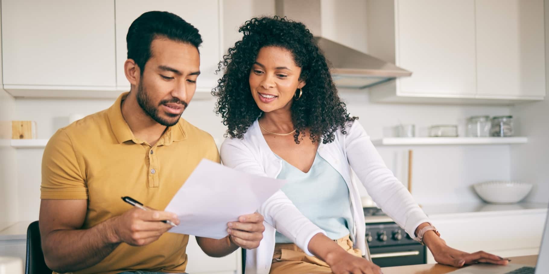 A happy diverse couple sitting at their kitchen counter reviewing paperwork.