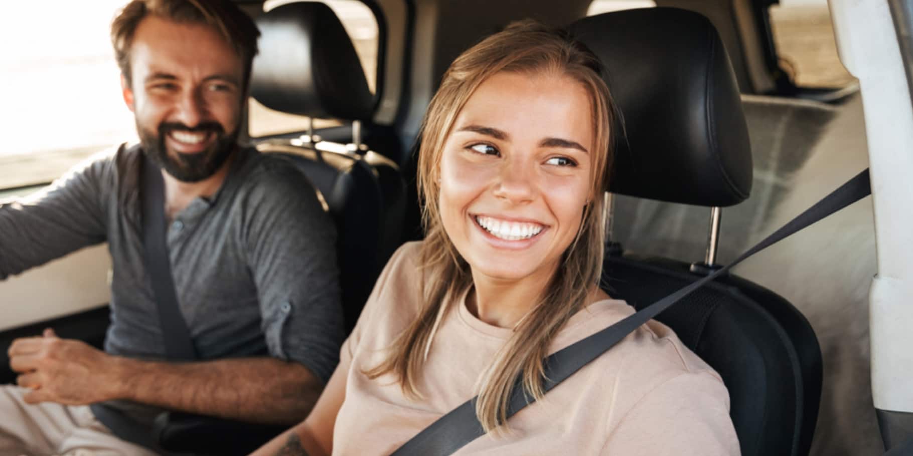 Smiling couple wearing seat belts sit together in a vehicle during a drive.