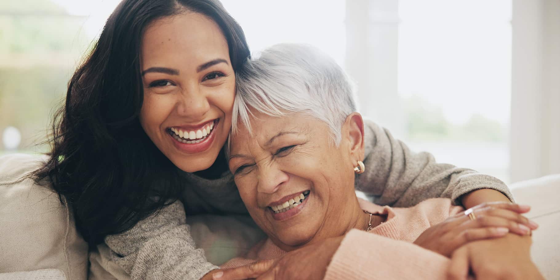 A smiling woman embracing a smiling, elderly woman.