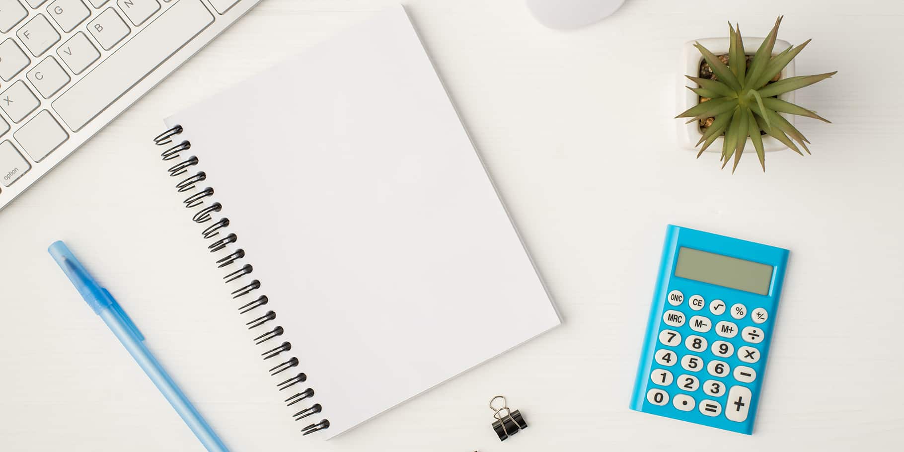 A calculator resting on a desk along with a notebook and a keyboard.